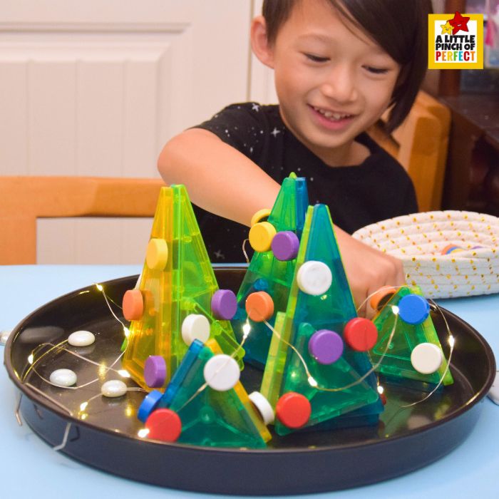Child adding magnetic ornaments to a Magna-Tile Christmas Tree.