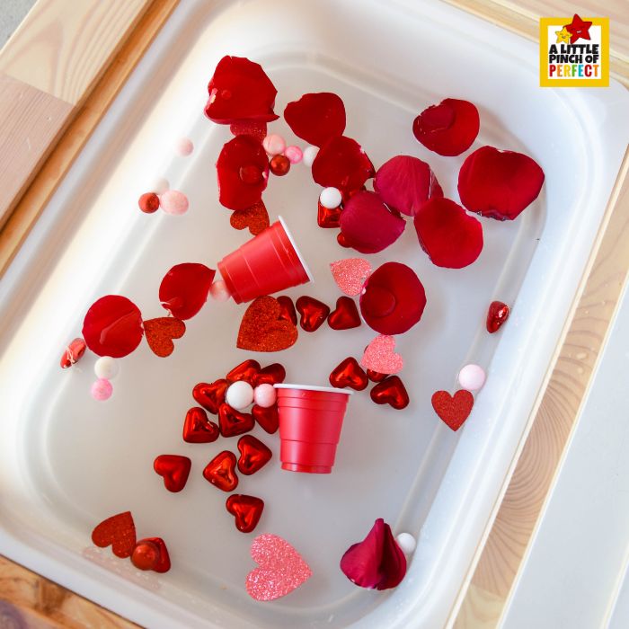 Love Potion Pour & Play Valentine Sensory Bin supply list with hearts, petals, foam balls, and sensory tools