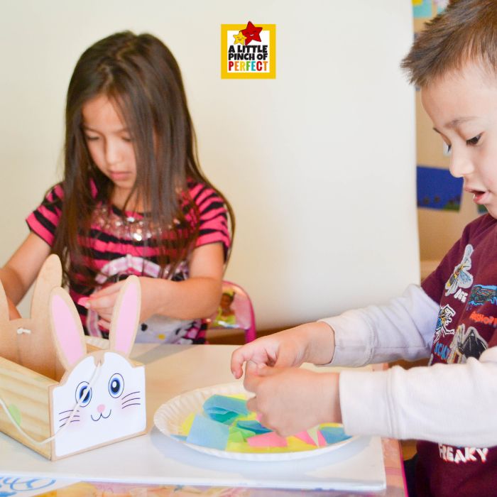What’s Inside the Easter Egg? Easter Egg Suncatcher Craft for Kids (Free Template) – kids placing colorful tissue paper squares onto sticky contact paper to create mosaic effect