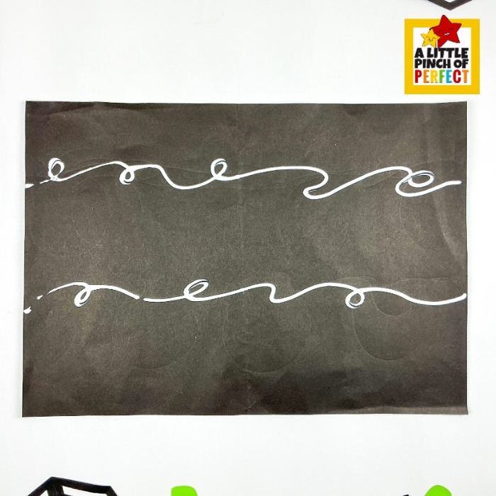 Apple stamped pumpkin patch Halloween art project for kids, so easy kids can help with every single step! Two wavy lines of Elmer's glue are drawn horizontally across black paper as guides for placing the green yarn vines, setting the stage for a spooky and creative pumpkin patch scene.