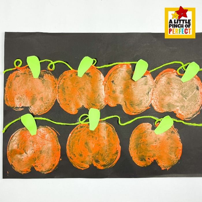 Apple stamped pumpkin patch Halloween art project for kids, a fun fall craft that turns simple materials into stunning seasonal artwork for any age! Green paper leaf shapes are glued to the top of each orange pumpkin print, adding a sweet foliage finishing touch to this easy homeschool or classroom Halloween art project.