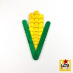popsicle stick corn craft — a perfect harvest season project for kids, homeschool art lessons, or fall classroom decorations, with the completed corn on the cob showing off its yellow kernel body, hand-drawn kernel rows, and green husk framing for a festive seasonal look.